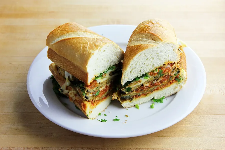 A cross-section of an eggplant parmesan sandwich on a plate.