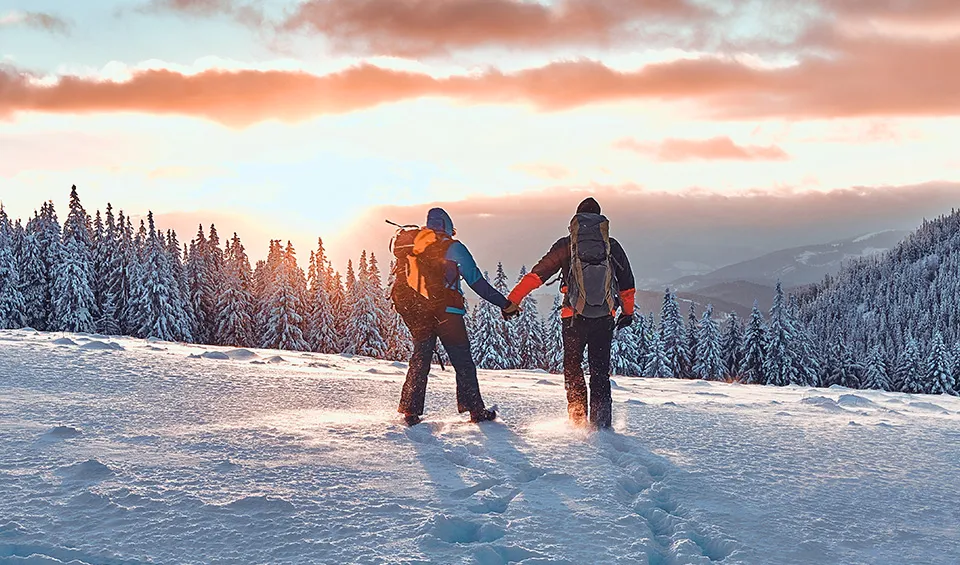 Two people holding hands hiking over snow