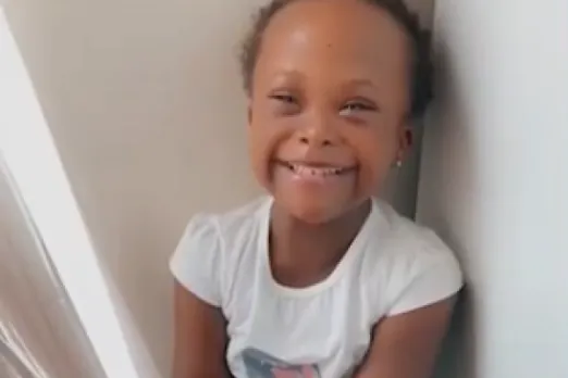 A little girl named Feyisayo smiles brightly while sitting on the floor after being treated at UMass Memorial Health.